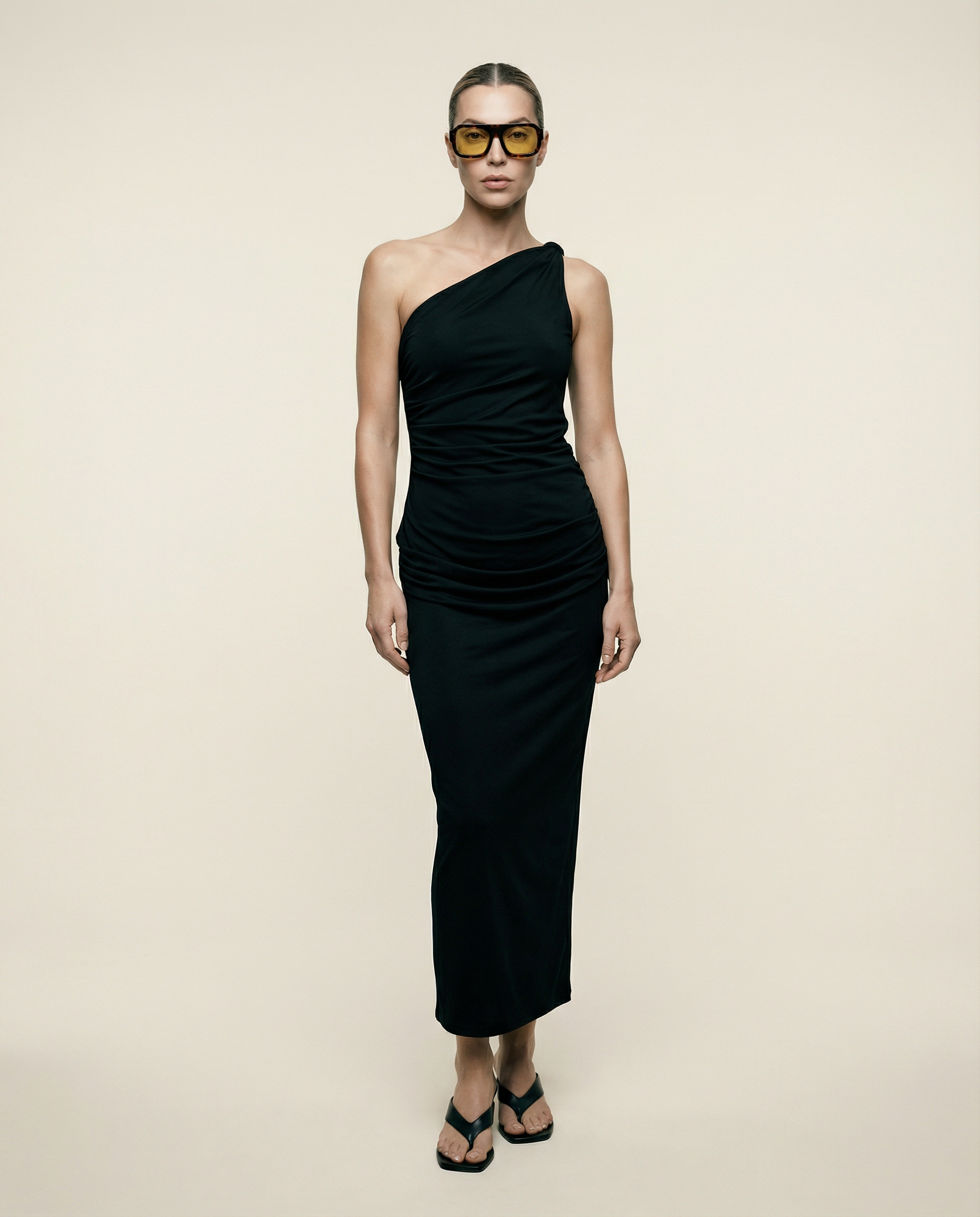 Woman wearing a black one-shoulder dress against a beige background