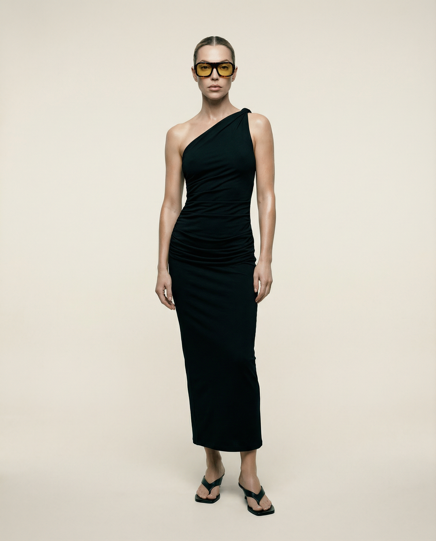 Woman wearing a black one-shoulder dress against a beige background