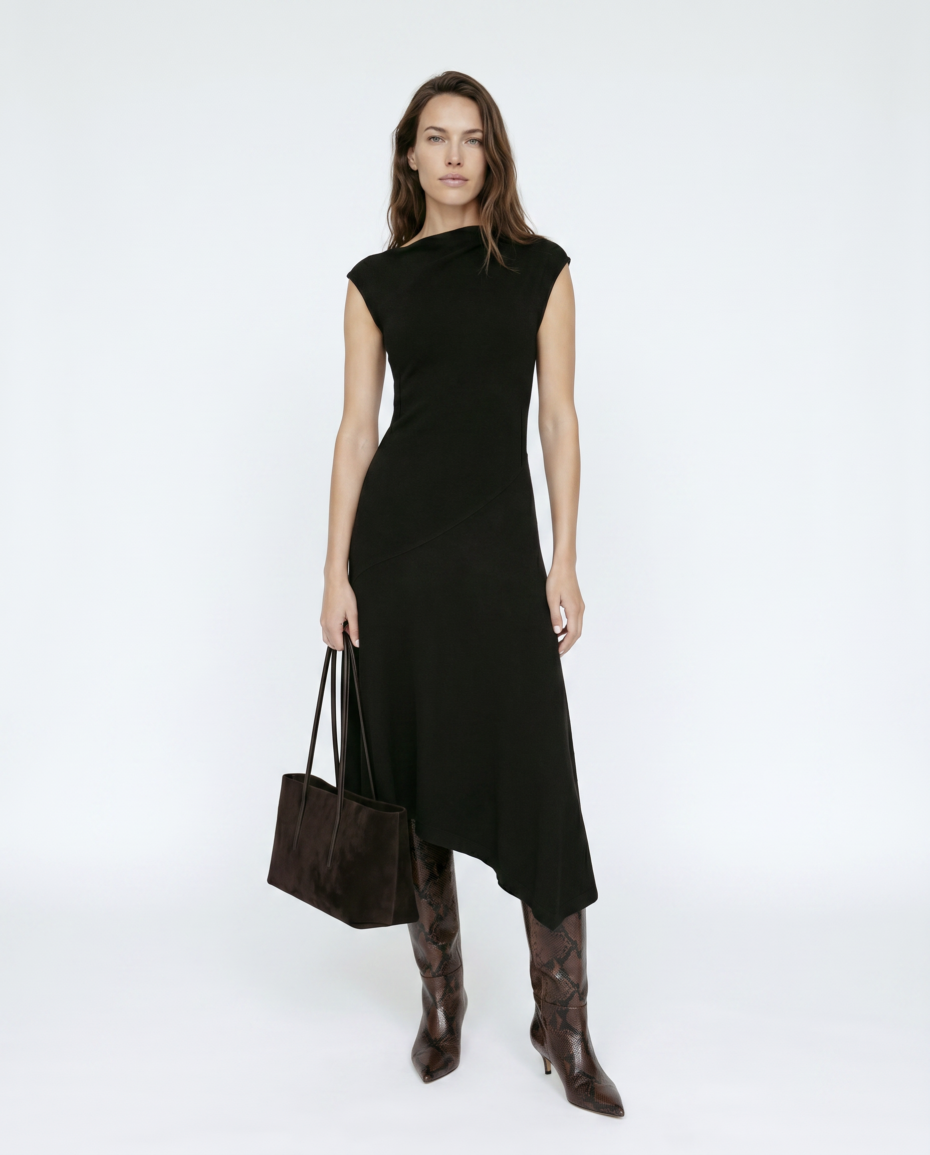 Woman wearing a black dress with brown boots and a handbag on a white background