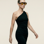 Woman wearing a black one-shoulder dress and sunglasses on a beige background