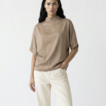 Woman wearing a beige top and white pants with brown boots on a white background