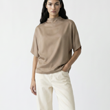 Woman wearing a beige top and white pants with brown boots on a white background