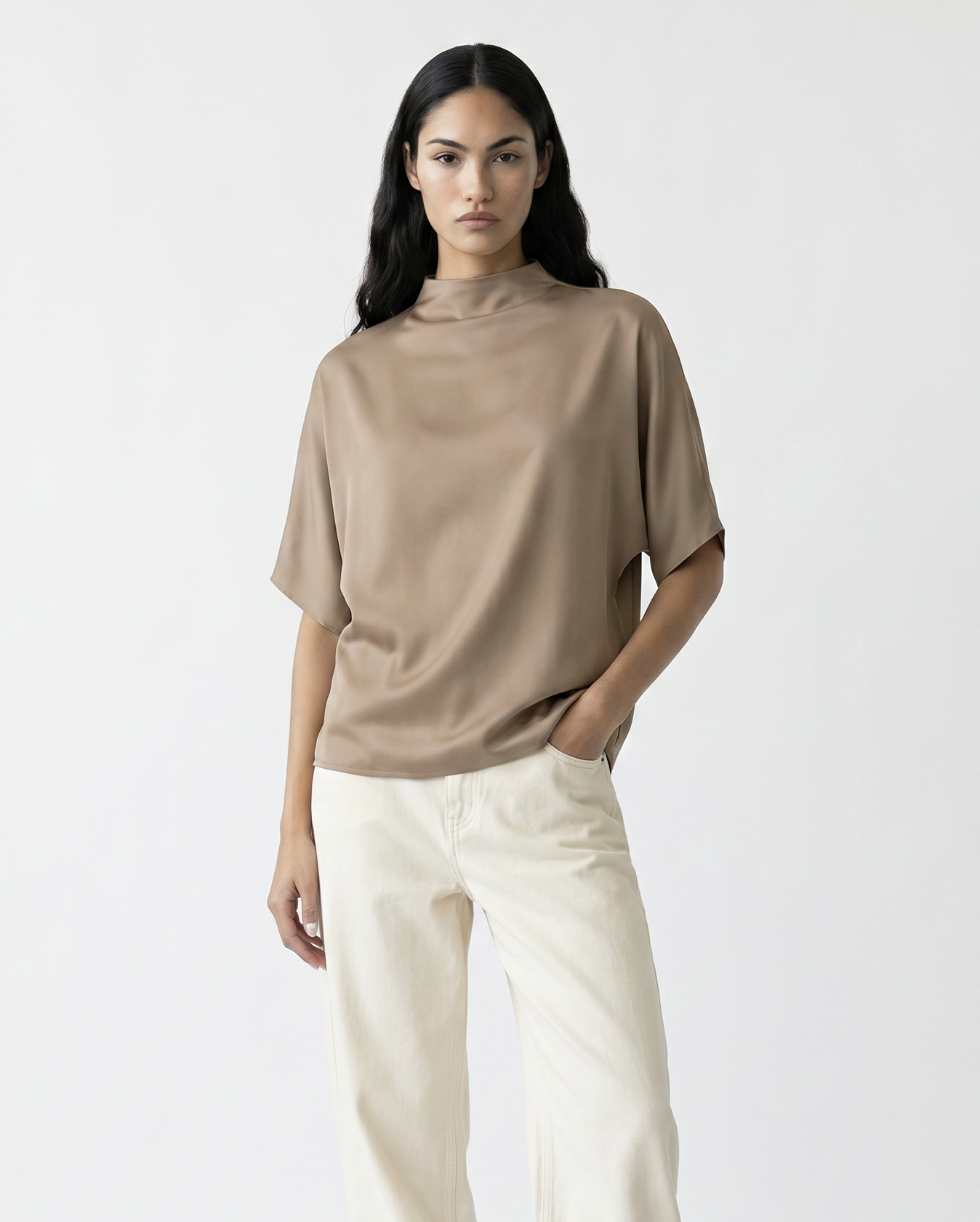 Woman wearing a beige top and white pants with brown boots on a white background