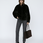 Person wearing a black jacket, gray pants, and holding a black bag on a white background