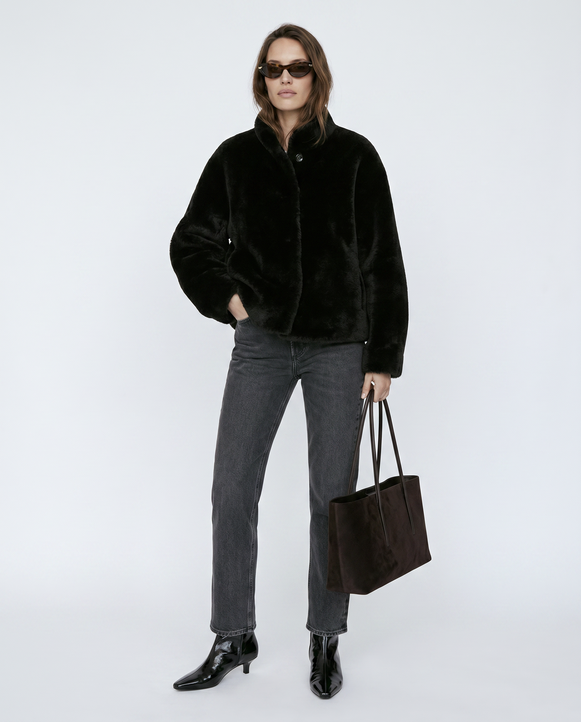 Person wearing a black jacket, gray pants, and holding a black bag on a white background