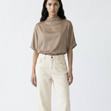 Woman wearing a beige top and white pants with brown boots on a white background