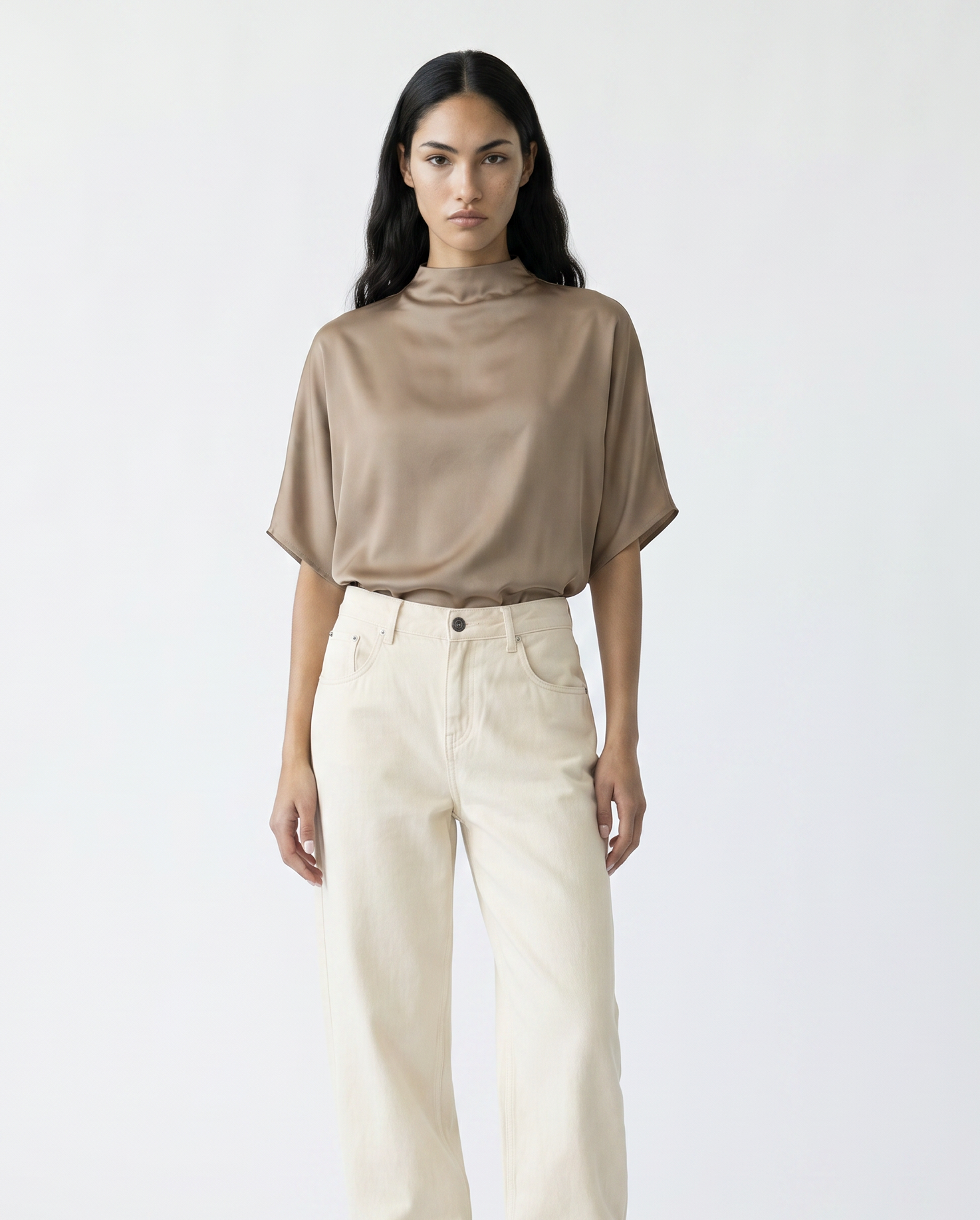 Woman wearing a beige top and white pants with brown boots on a white background