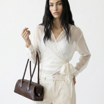 Woman in a white outfit holding a brown handbag against a white background