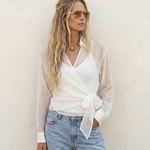 Woman wearing a white blouse with sheer sleeves and light blue jeans against a plain background