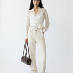 Woman wearing a white outfit with a belt, holding a brown bag on a white background