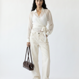 Woman wearing a white outfit with a belt, holding a brown bag on a white background