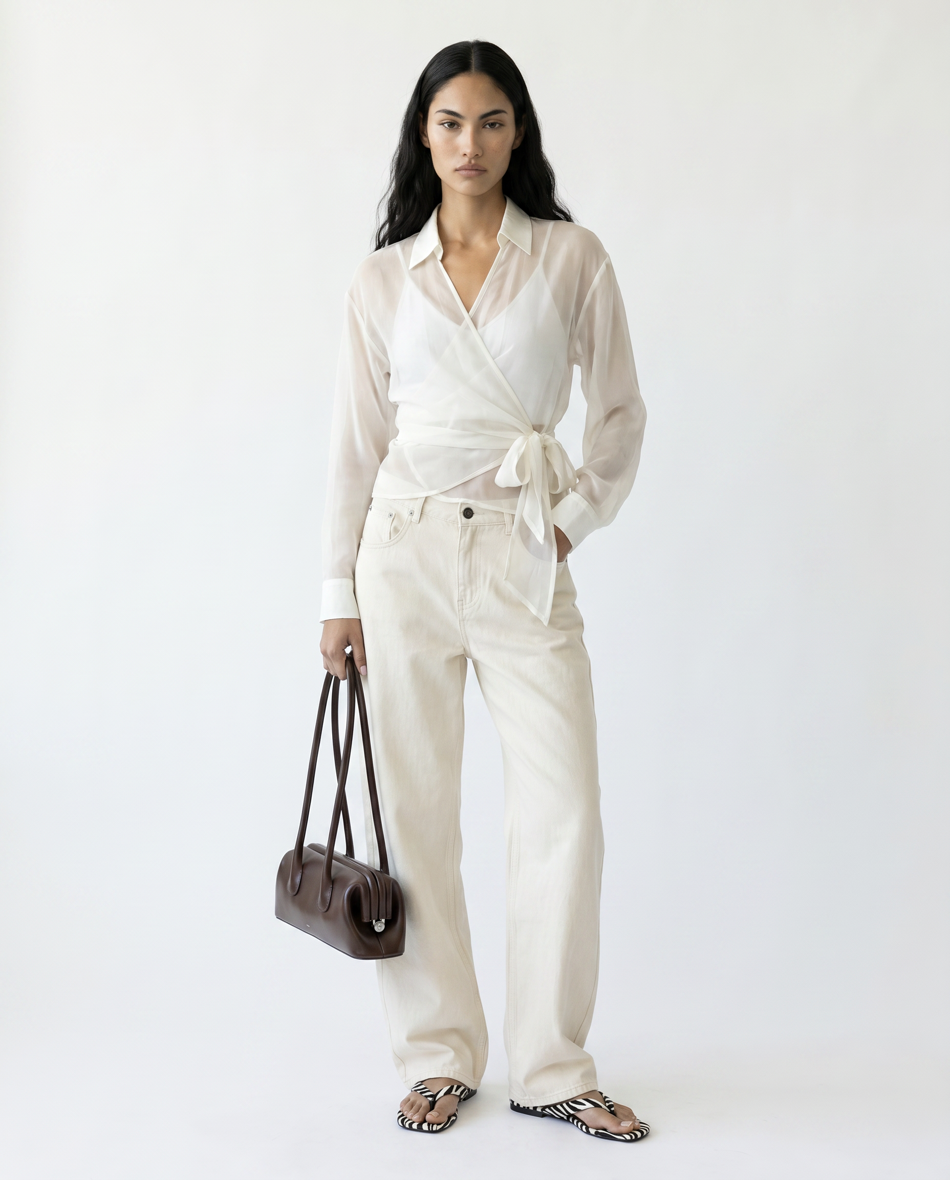 Woman wearing a white outfit with a belt, holding a brown bag on a white background