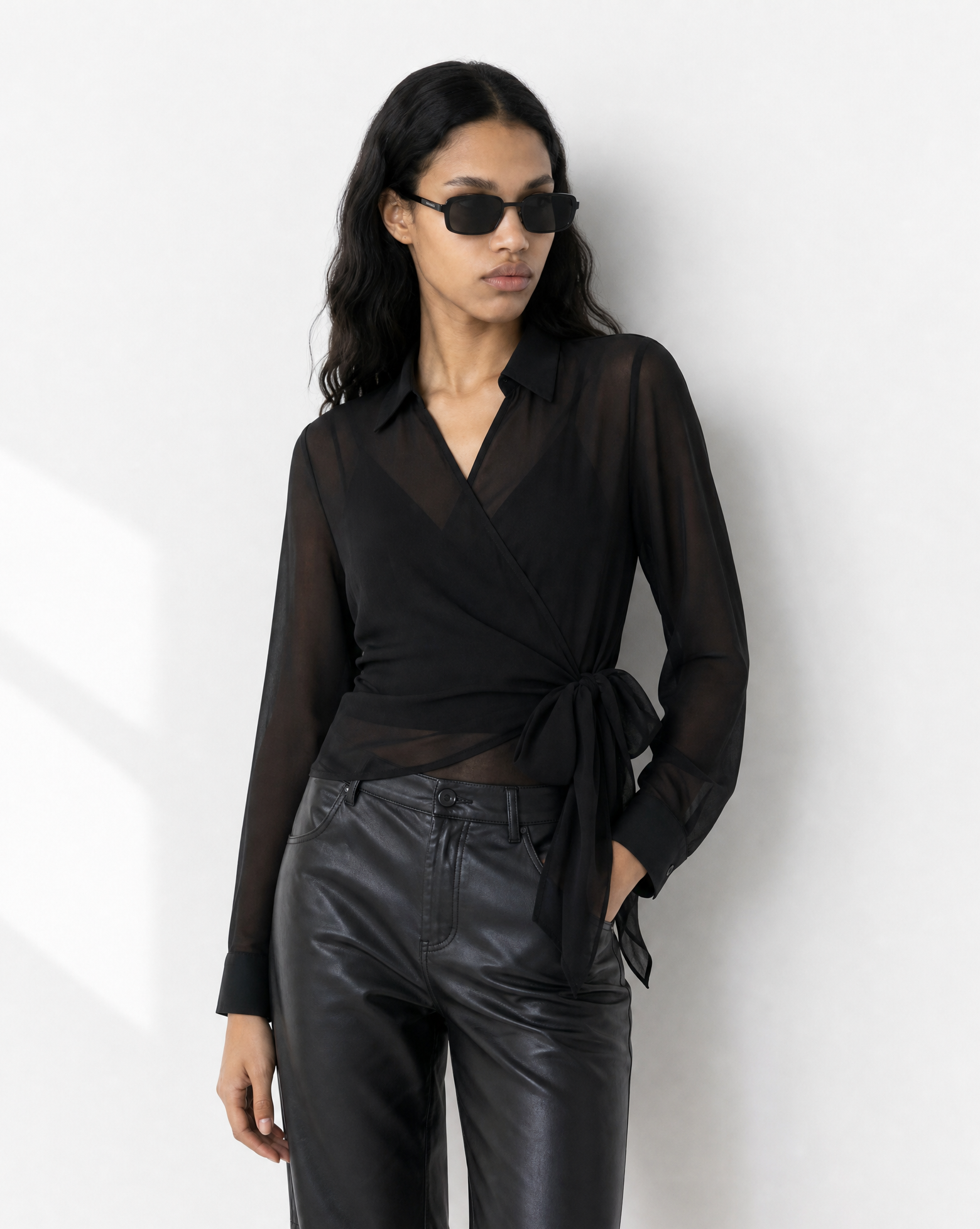 Woman wearing a black blouse and leather shorts with sunglasses on a white background