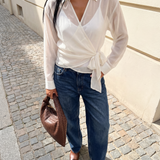 Person wearing a white blouse, blue jeans, and brown shoes on a street.