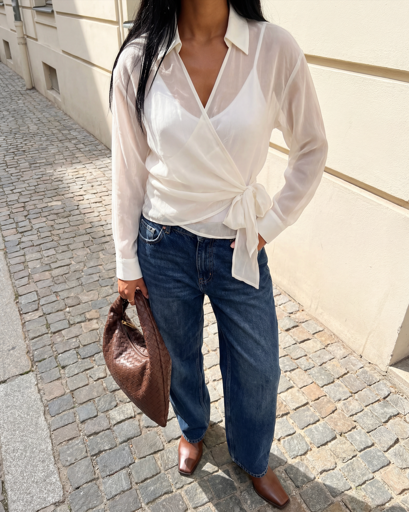 Person wearing a white blouse, blue jeans, and brown shoes on a street.