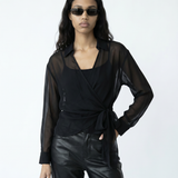 Woman wearing a black sheer top and leather pants with sunglasses on a white background