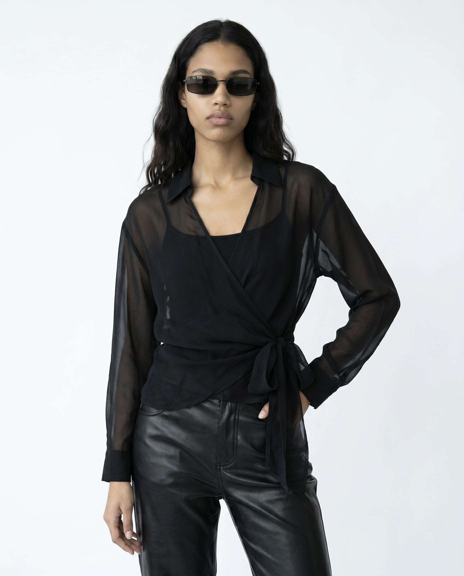 Woman wearing a black sheer top and leather pants with sunglasses on a white background