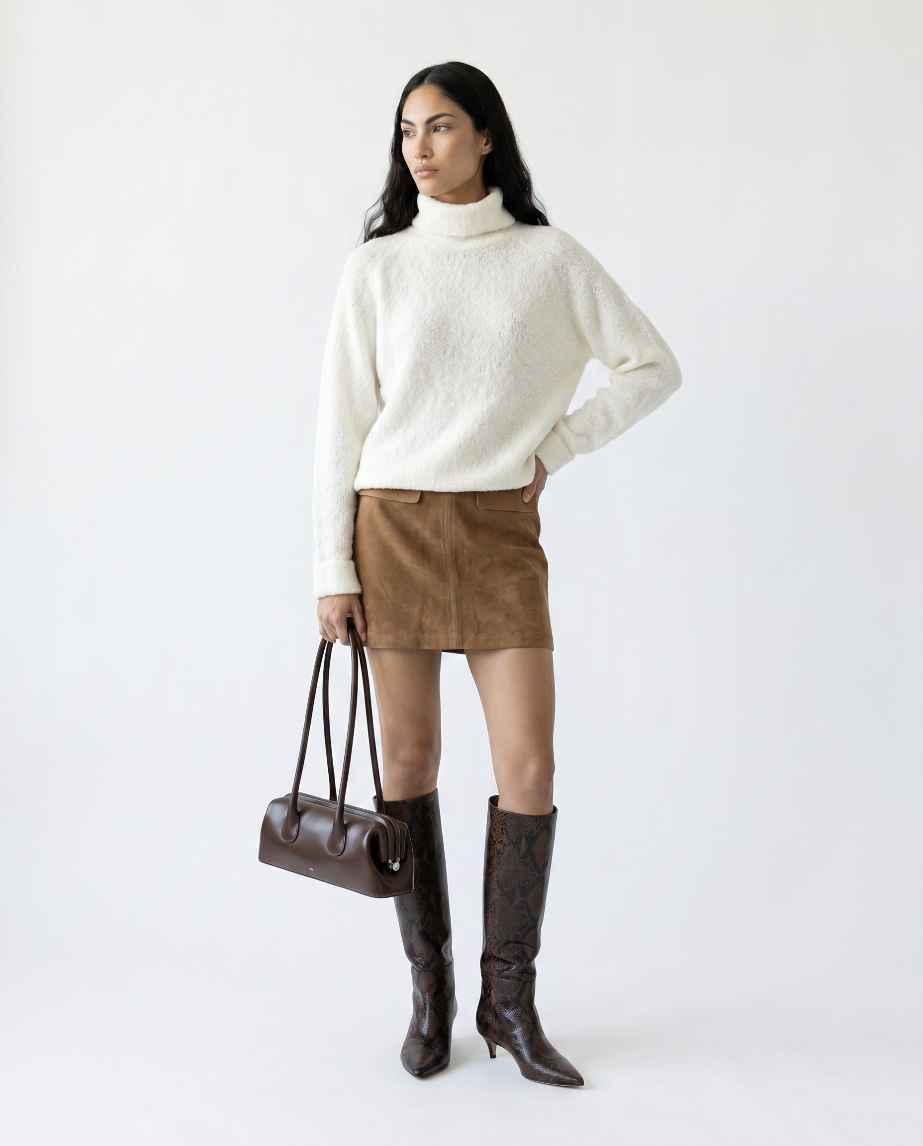 Woman wearing a white sweater, brown skirt, and knee-high boots holding a brown handbag on a white background