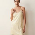 Woman wearing an ivory lace sequin dress against a plain background