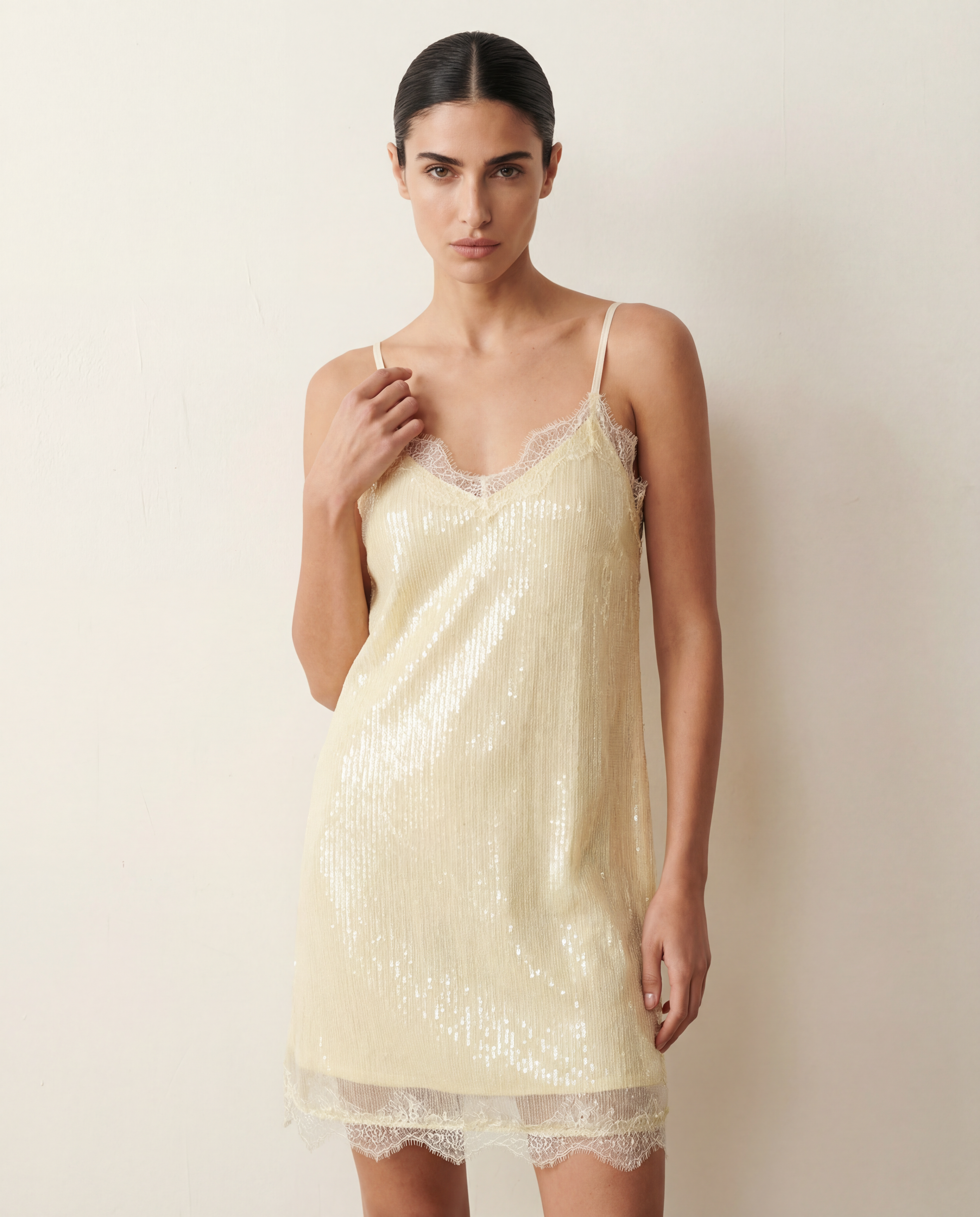 Woman wearing an ivory lace sequin dress against a plain background