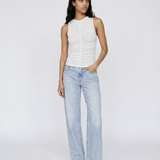 A model stands against a light gray studio background wearing a white sleeveless ruched top, light-wash wide-leg jeans, and leopard-print sandals.