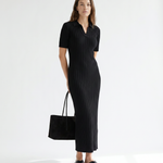 Woman wearing a black ribbed dress holding a matching black handbag on a white background