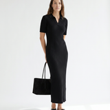 Woman wearing a black ribbed dress holding a matching black handbag on a white background