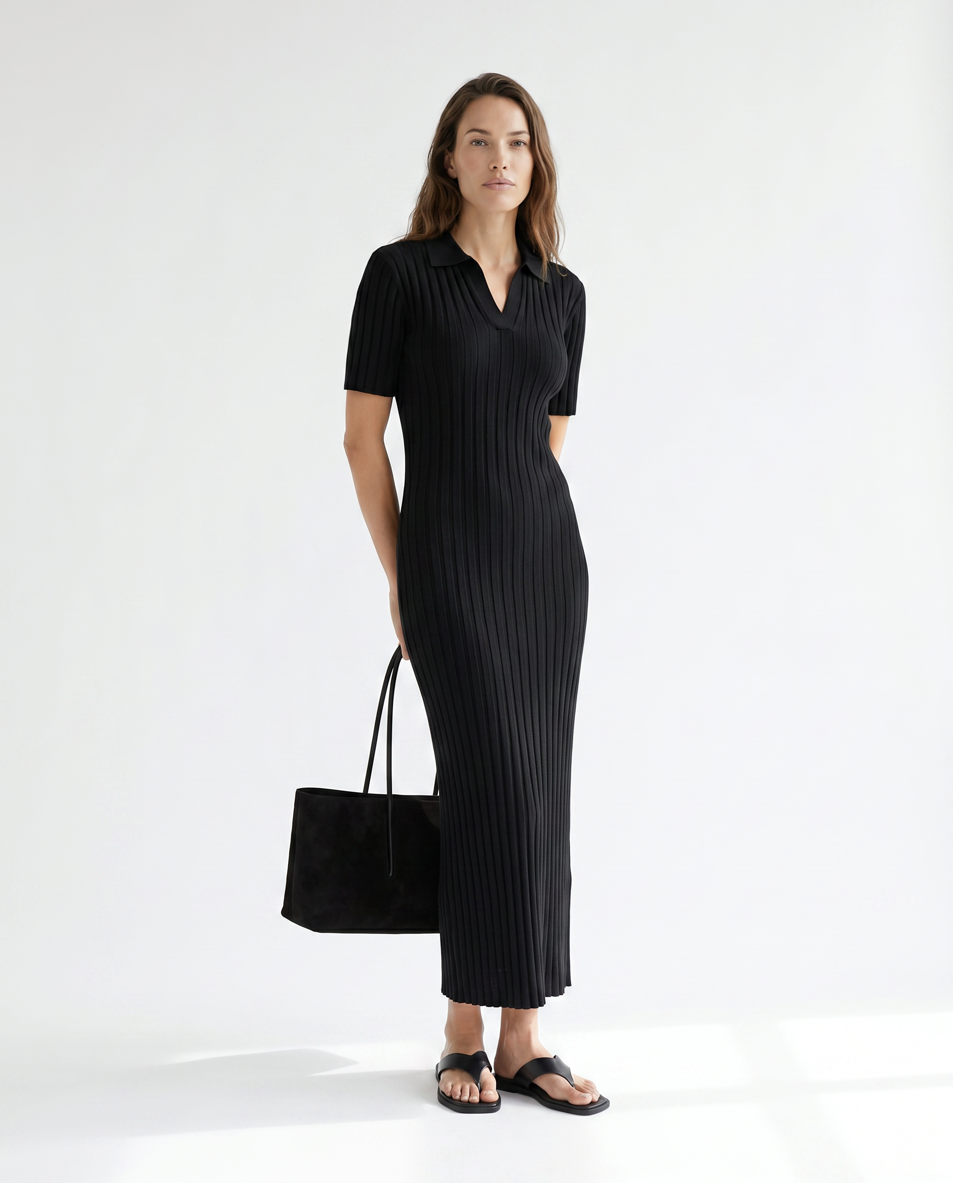 Woman wearing a black ribbed dress holding a matching black handbag on a white background