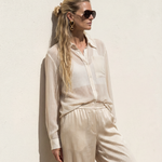 Woman wearing a light-colored outfit with sunglasses against a plain background