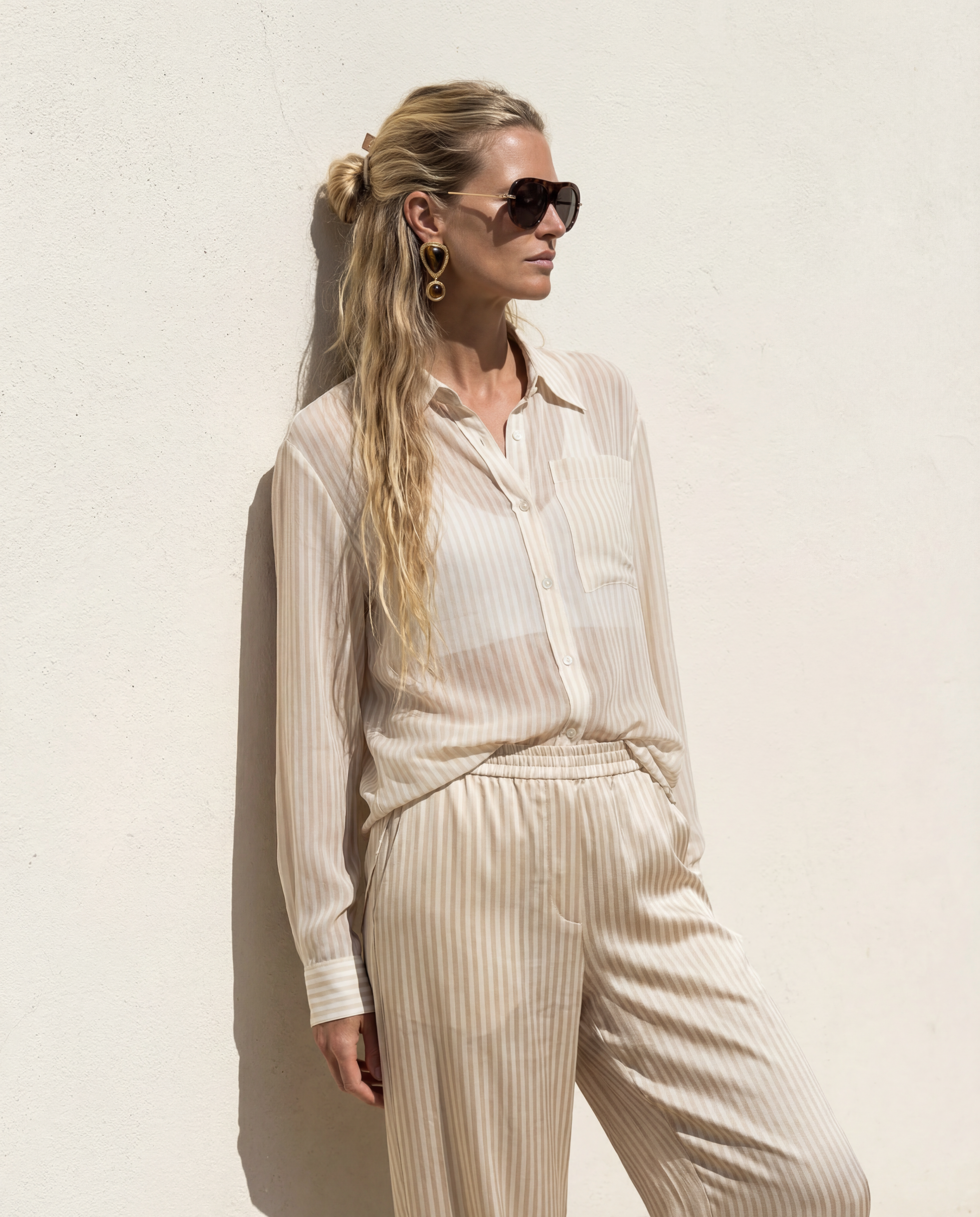 Woman wearing a light-colored outfit with sunglasses against a plain background