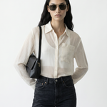Woman wearing a white striped shirt, black pants, and sunglasses with a black bag on a white background