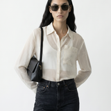 Woman wearing a white striped shirt, black pants, and sunglasses with a black bag on a white background