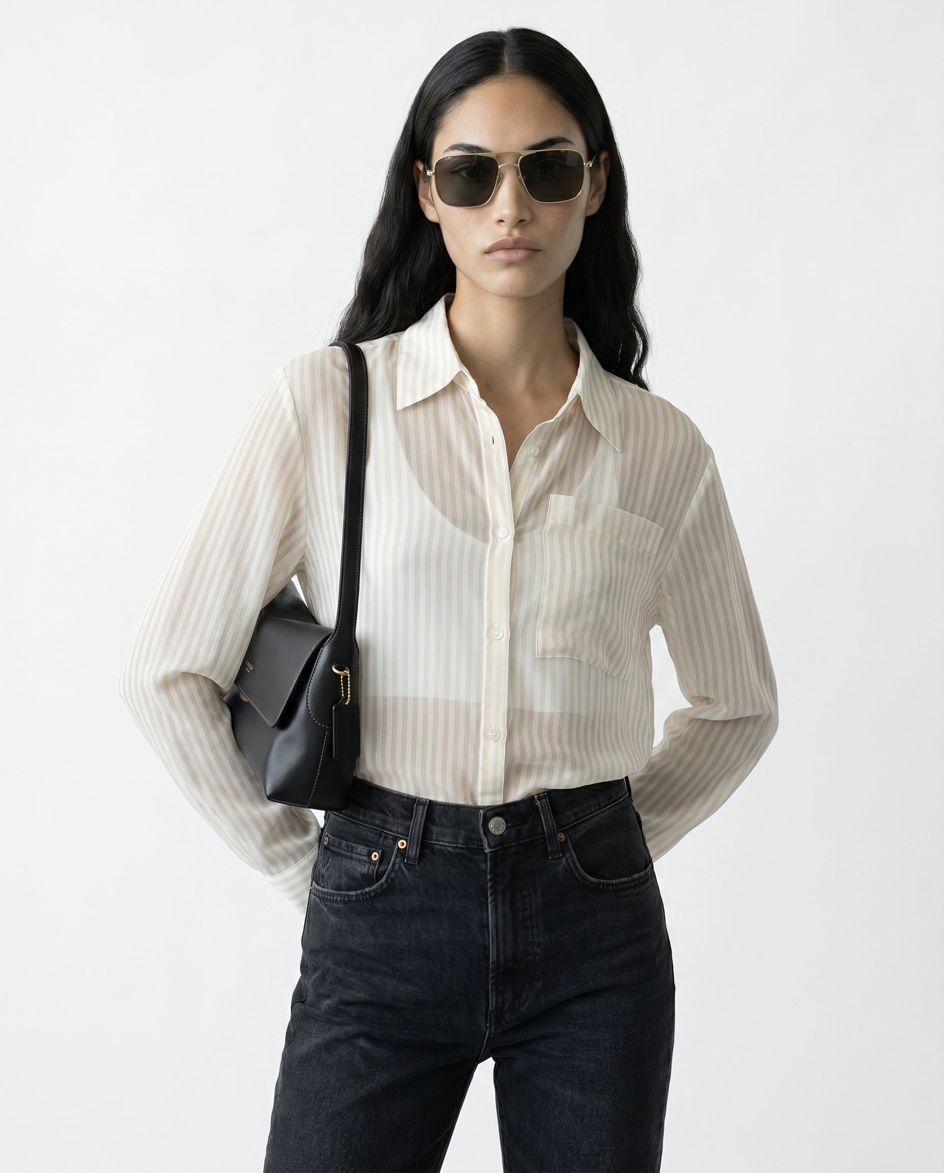 Woman wearing a white striped shirt, black pants, and sunglasses with a black bag on a white background