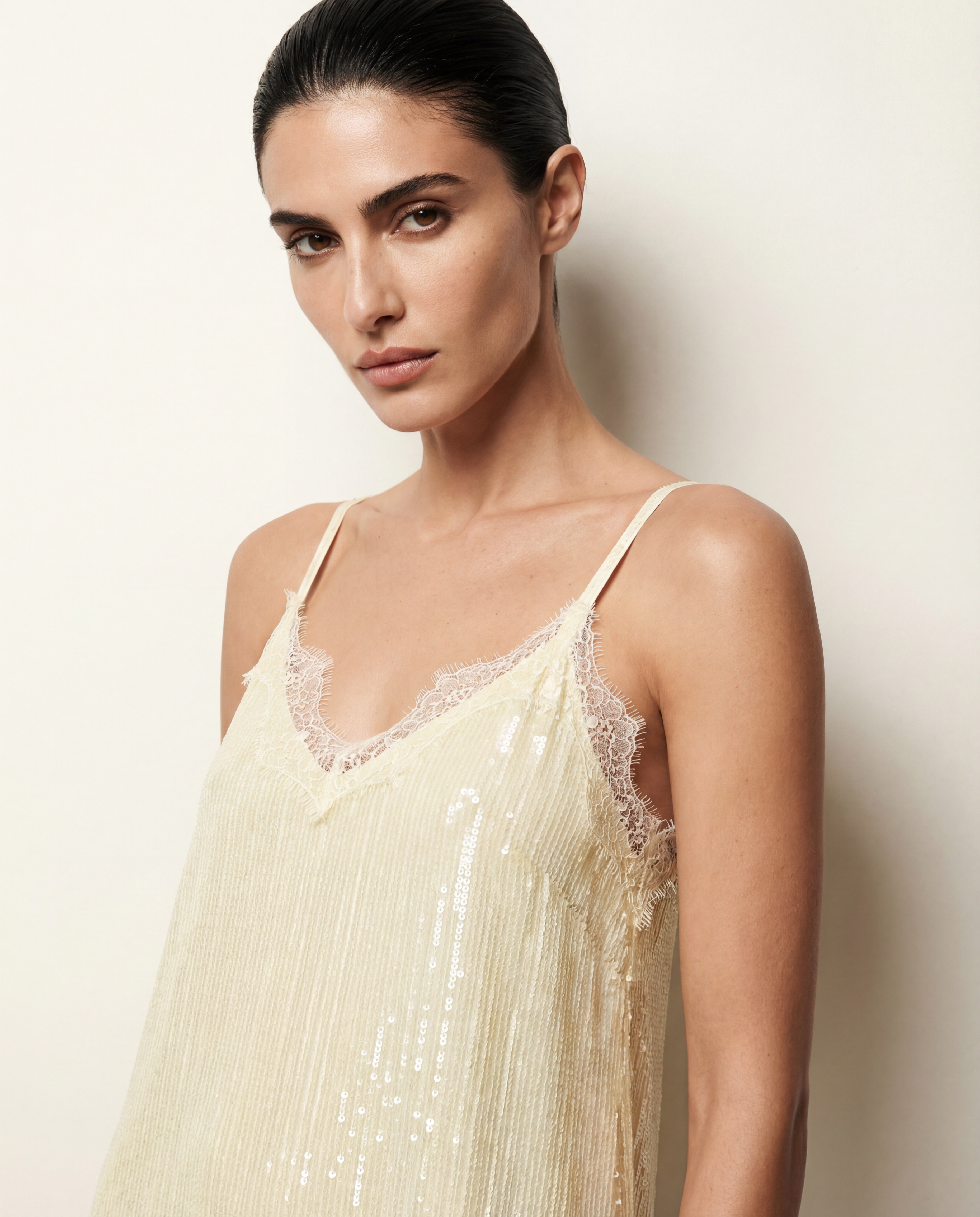 Woman wearing a beige lace-trimmed top against a plain background