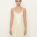Woman wearing a light yellow sequin slip dress against a white background