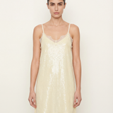 Woman wearing a light yellow sequin slip dress against a white background