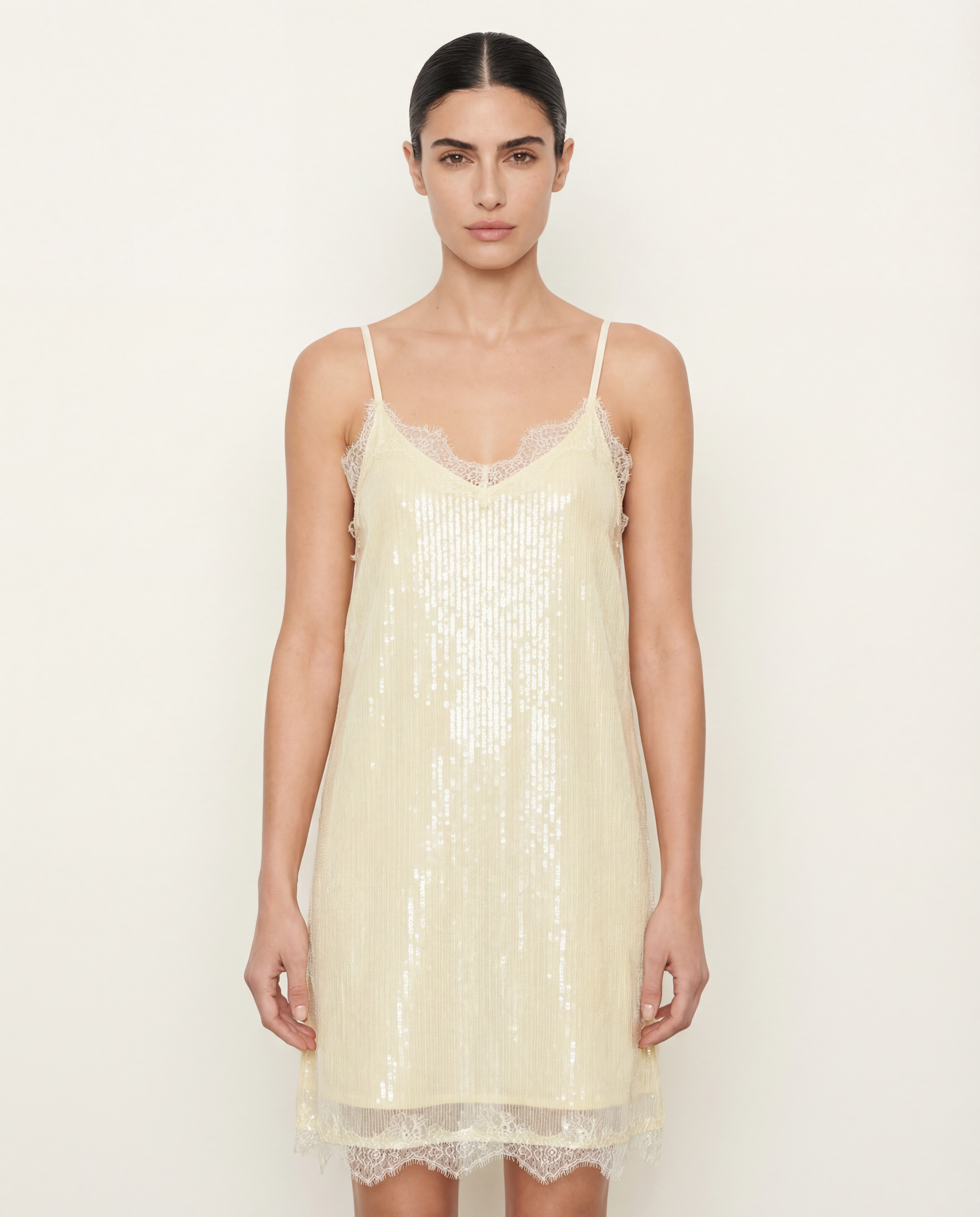 Woman wearing a light yellow sequin slip dress against a white background