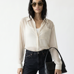 Woman wearing a white shirt, black jeans, and sunglasses, holding a black handbag on a white background