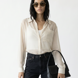 Woman wearing a white shirt, black jeans, and sunglasses, holding a black handbag on a white background