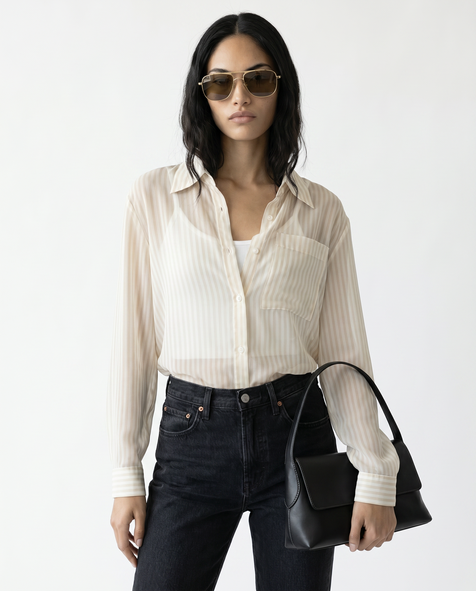 Woman wearing a white shirt, black jeans, and sunglasses, holding a black handbag on a white background
