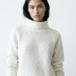 Woman wearing a textured white sweater against a plain background