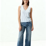 Woman wearing a light blue sleeveless top and wide-leg jeans on a white background