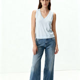 Woman wearing a light blue sleeveless top and wide-leg jeans on a white background