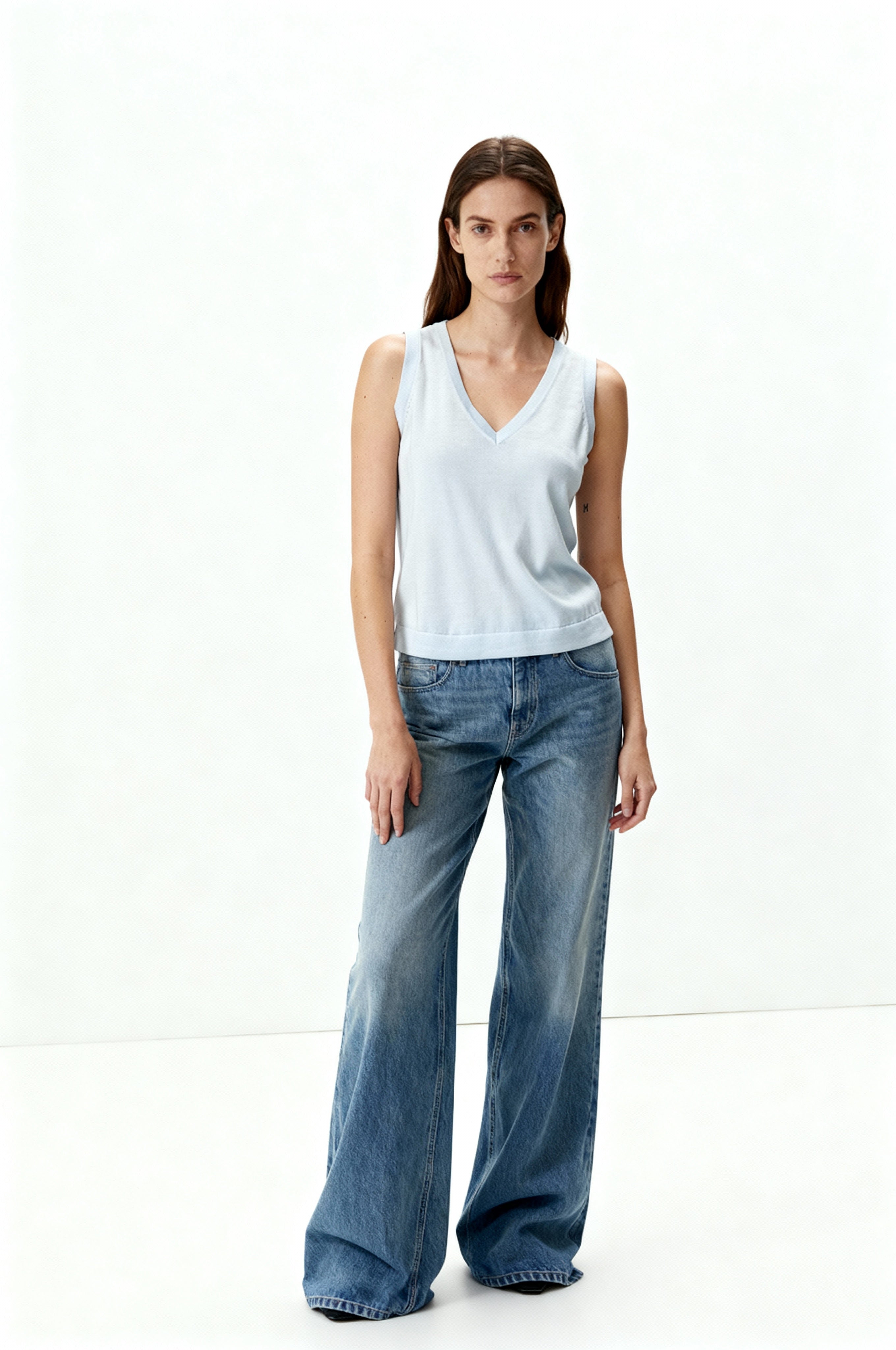Woman wearing a light blue sleeveless top and wide-leg jeans on a white background